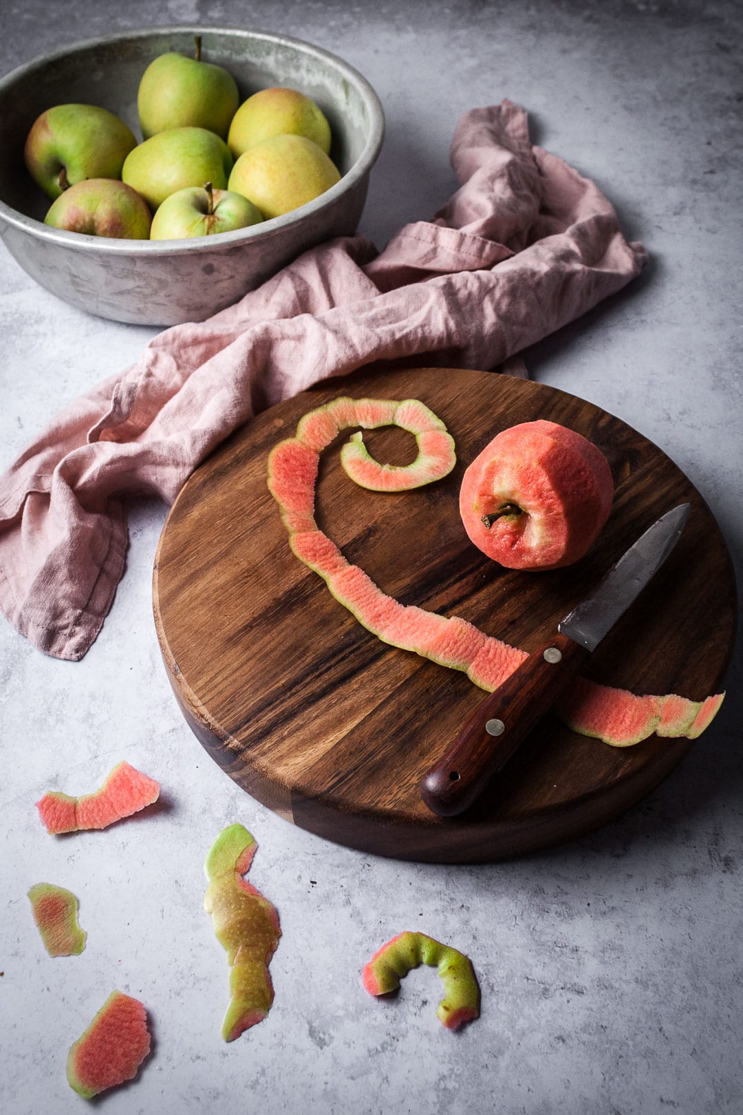 Peeled pink apple on a wooden cutting board and a grey background - prep shot for Pink Apple Tart with Cream Cheese Filling