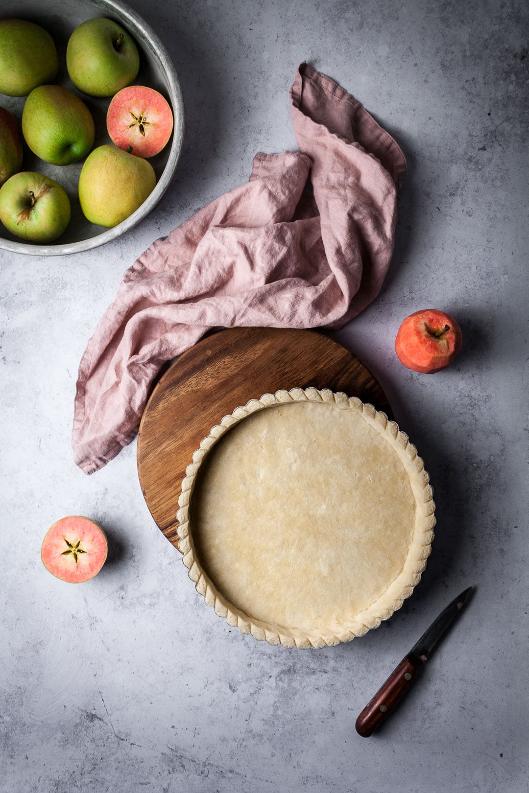 Tart shell for a Pink Apple Tart with cut pink apples and pink napkin nearby