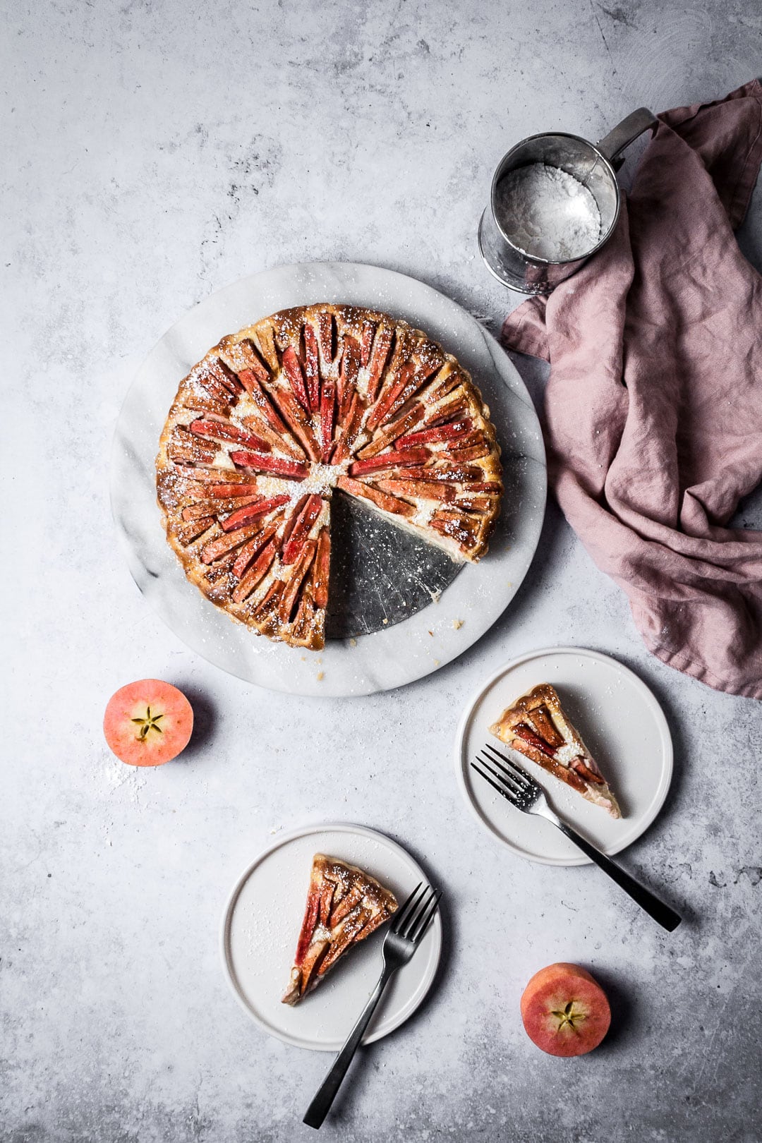 Two slices of Pink Apple Tart with Cream Cheese Filling on white plates with forks resting nearby; all on a grey background