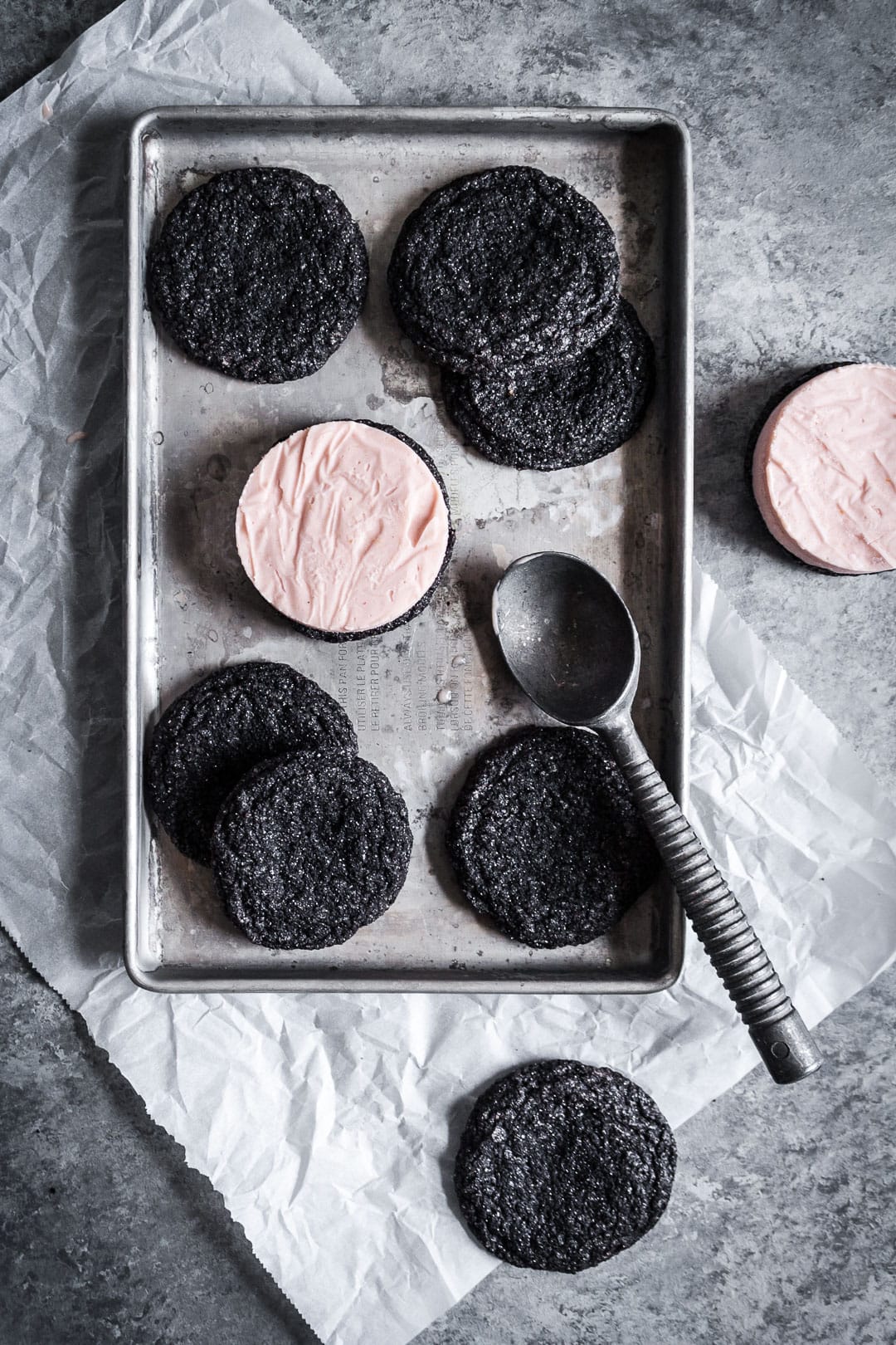 Process shot of chocolate blood orange ice cream sandwiches being built - cookies on silver tray with ice cream on top and ice cream scoop nearby