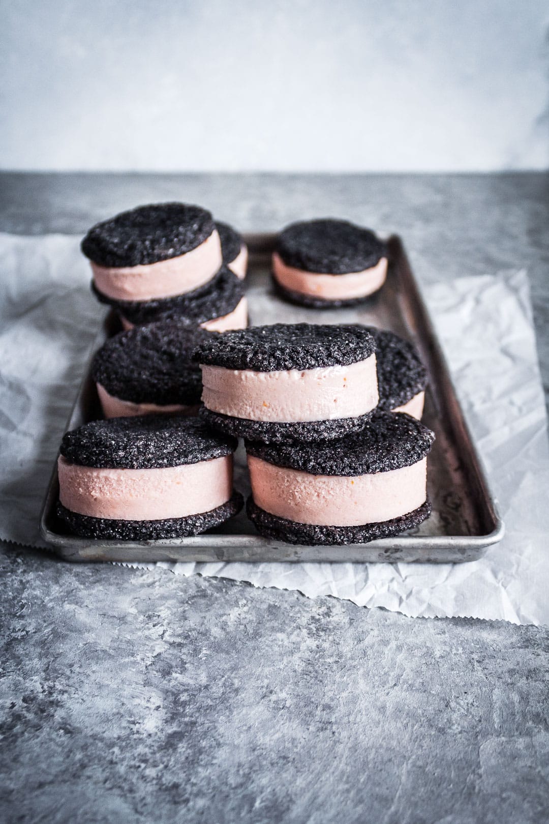 Chocolate blood orange ice cream sandwiches piled on a metal tray with parchment underneath on a grey background