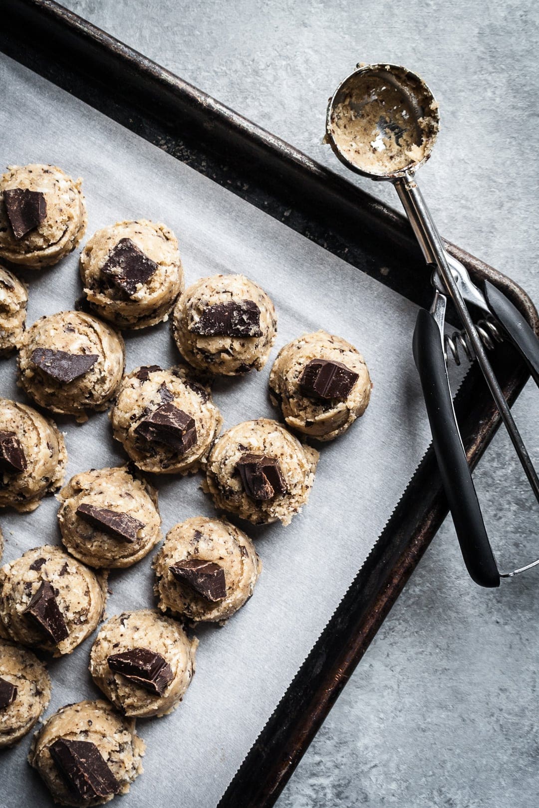 Top view of coconut chocolate chip cookie dough balls on a baking sheet with cookie scoop resting nearby