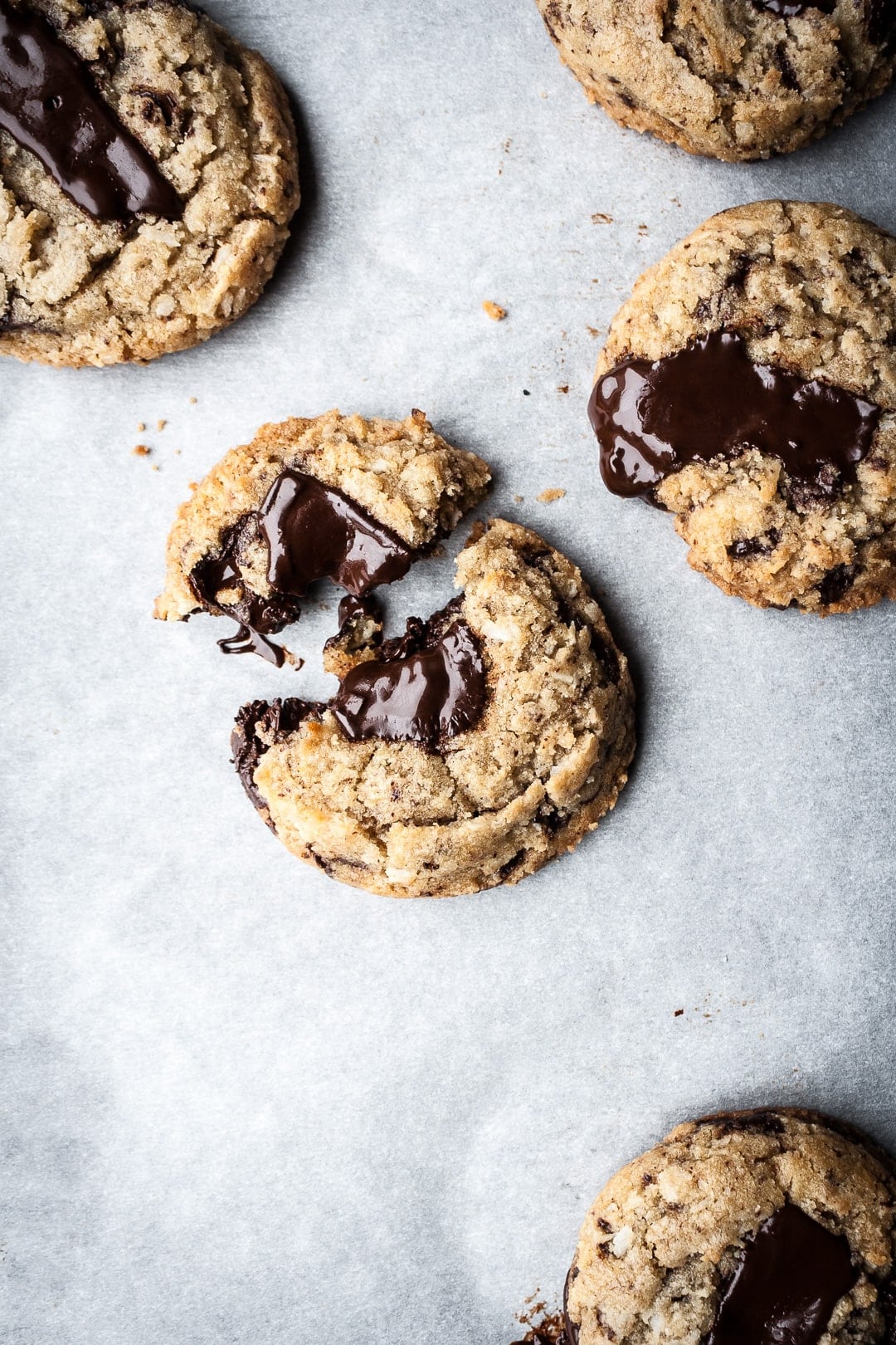 Top view of freshly baked coconut chocolate chip cookies with melted pools of chocolate resting on parchment paper