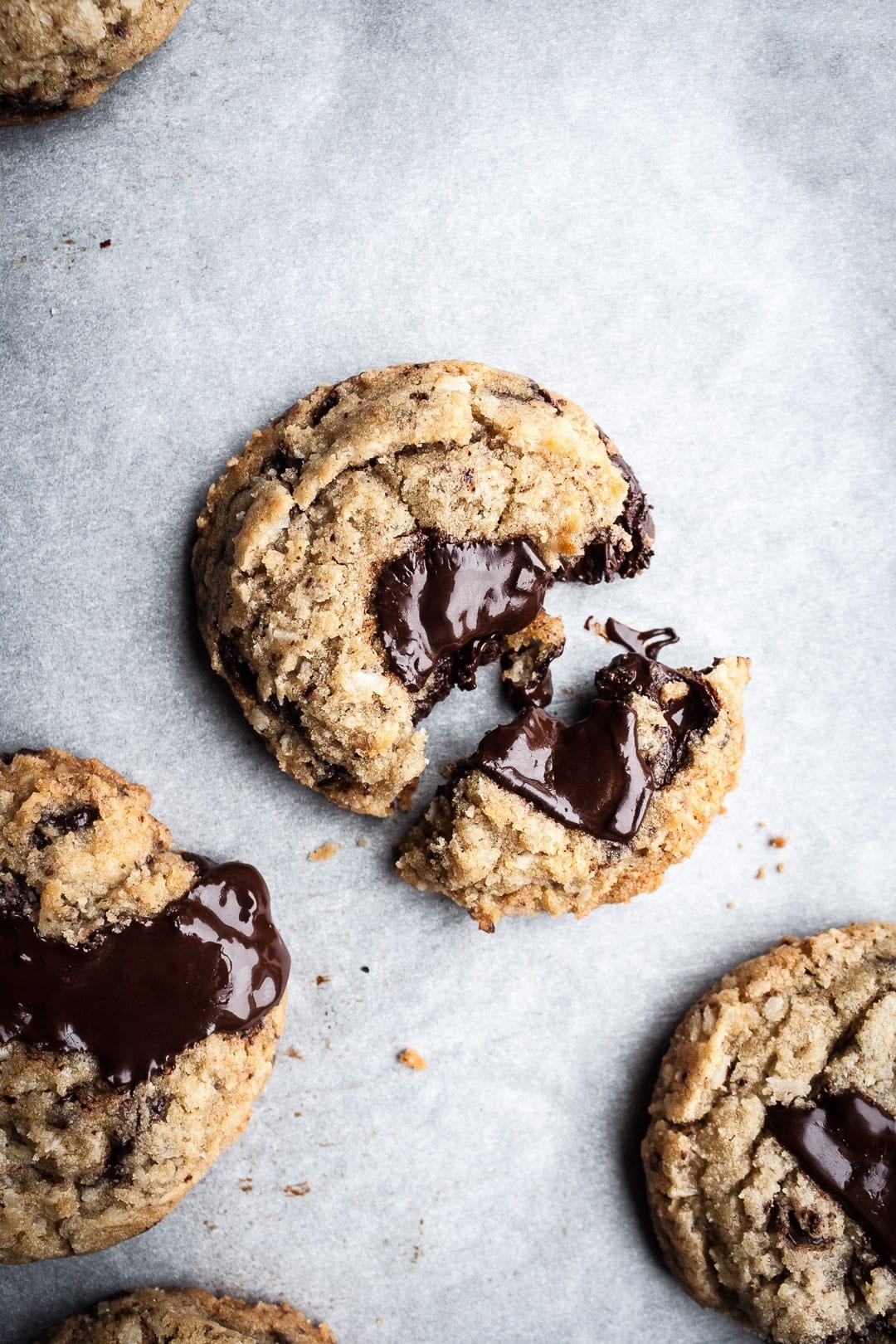 Top view of freshly baked coconut chocolate chip cookies with melted pools of chocolate resting on parchment paper