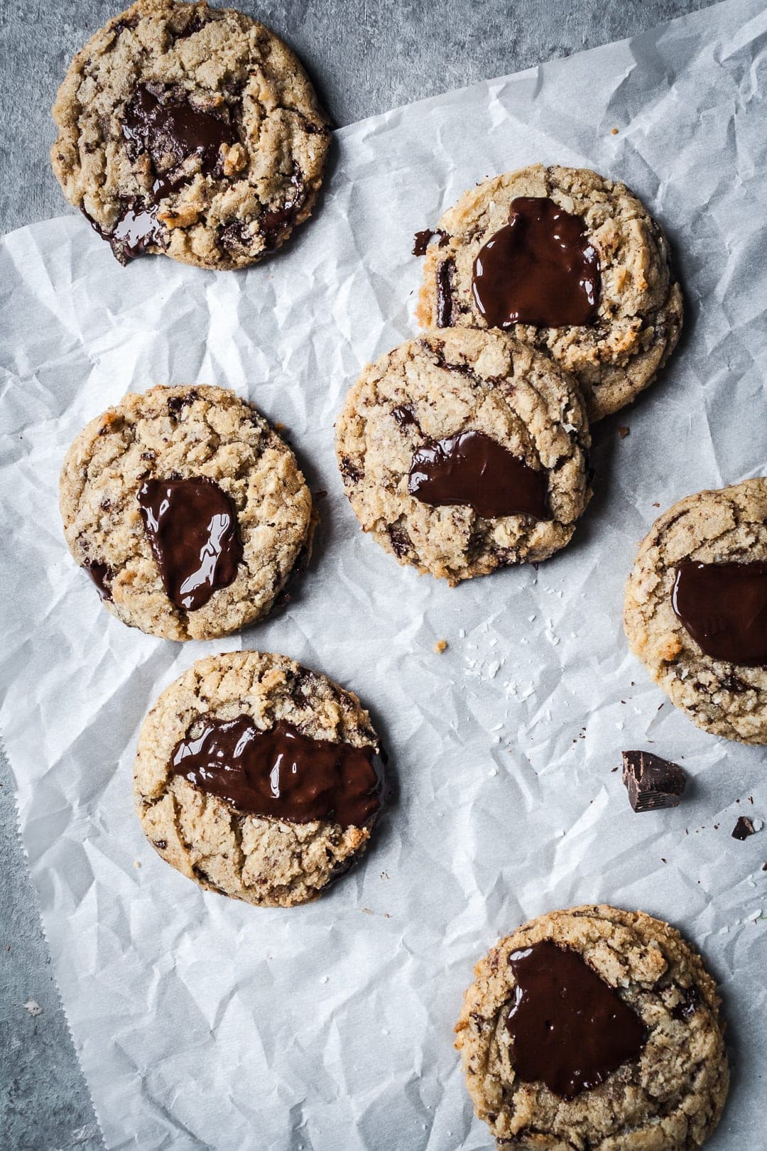 Top view of freshly baked coconut chocolate chip cookies with melted pools of chocolate resting on parchment paper