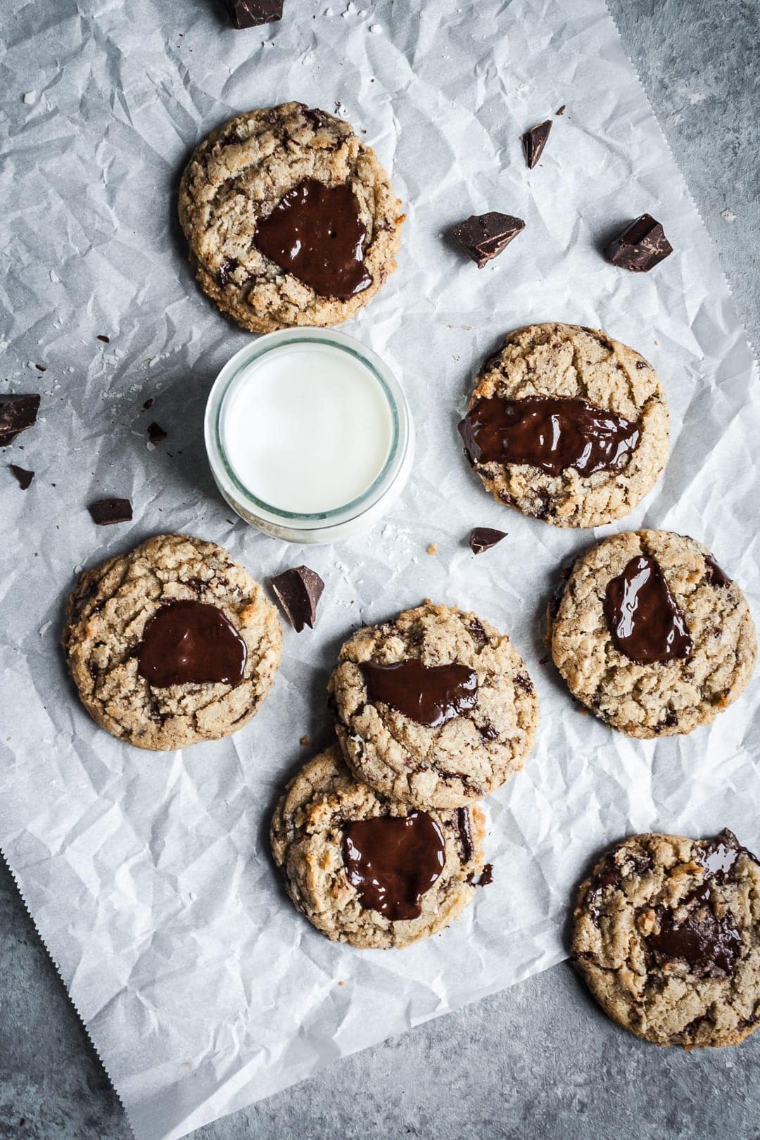 Top view of freshly baked coconut chocolate chip cookies with melted pools of chocolate with a glass of milk, resting on parchment paper