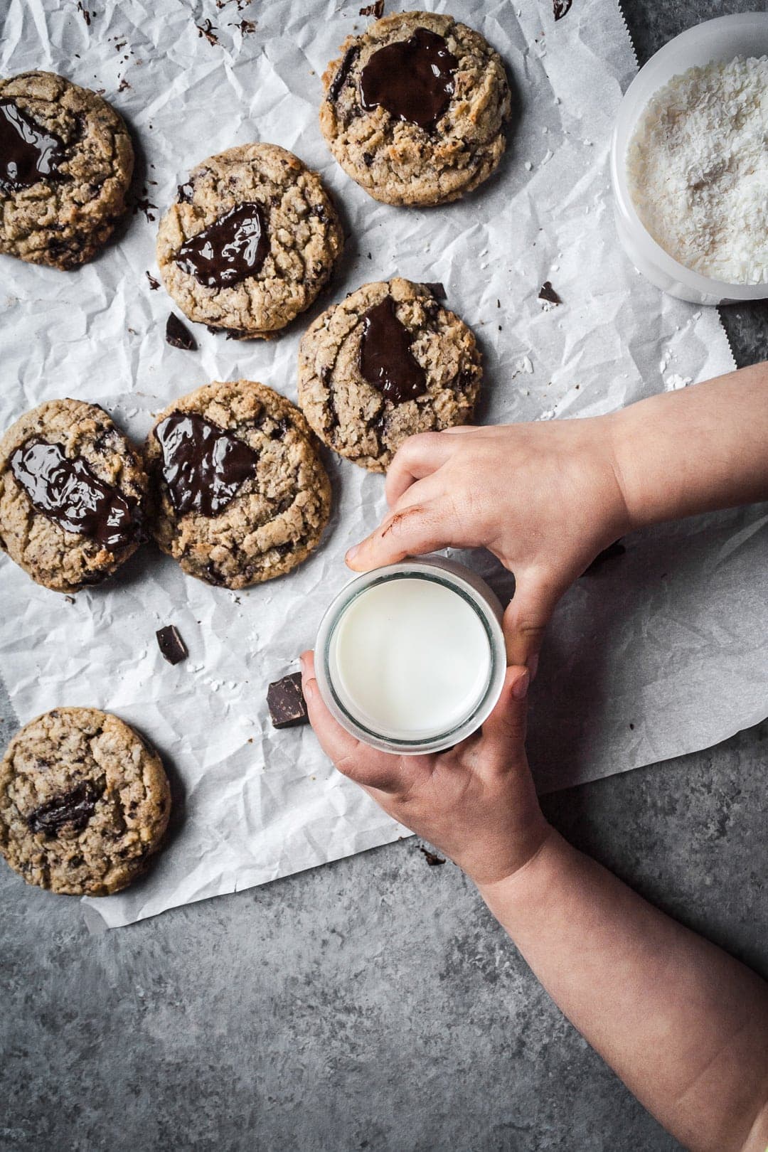 Top view of freshly baked coconut chocolate chip cookies with a child's hands holding a glass of milk