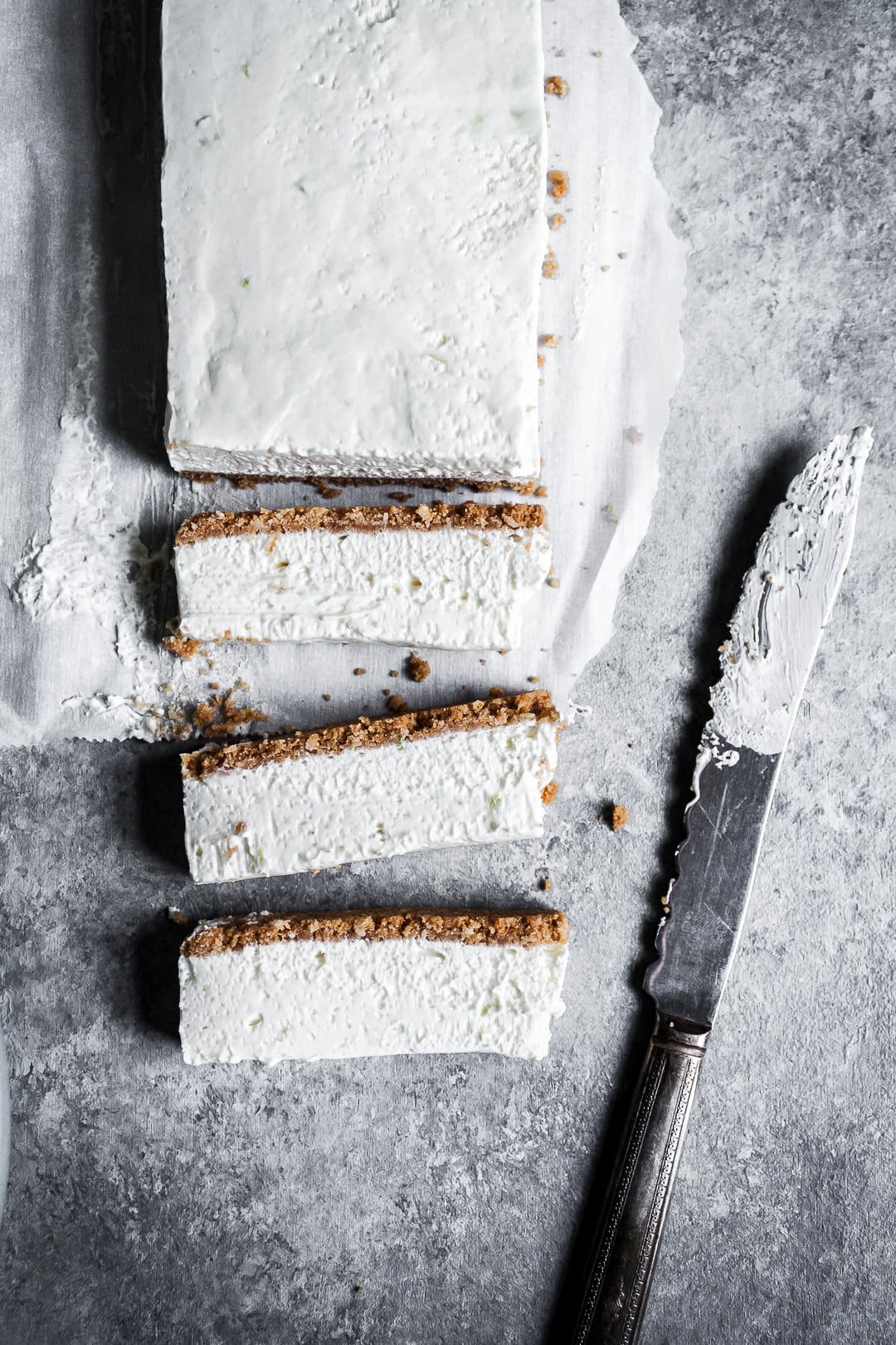 Key Lime Cheesecake Bars seen from above with three slices laying on their side next to a vintage knife on a grey background