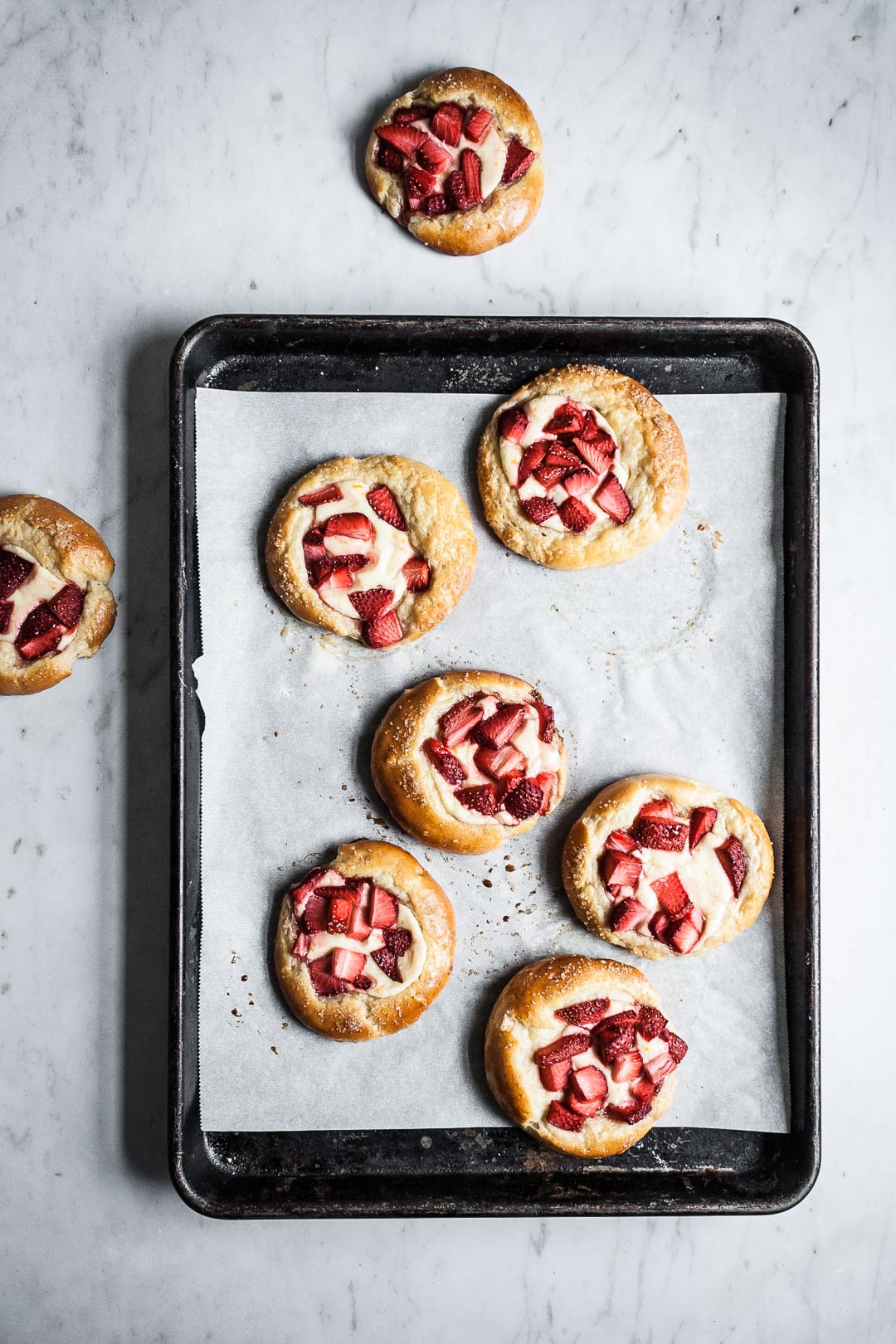 Brioche pastries on a black pan with white parchment resting on a marble background