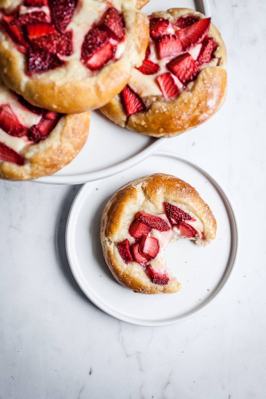 Brioche pastry on a white plate and marble background with more pastries piled on a plate nearby