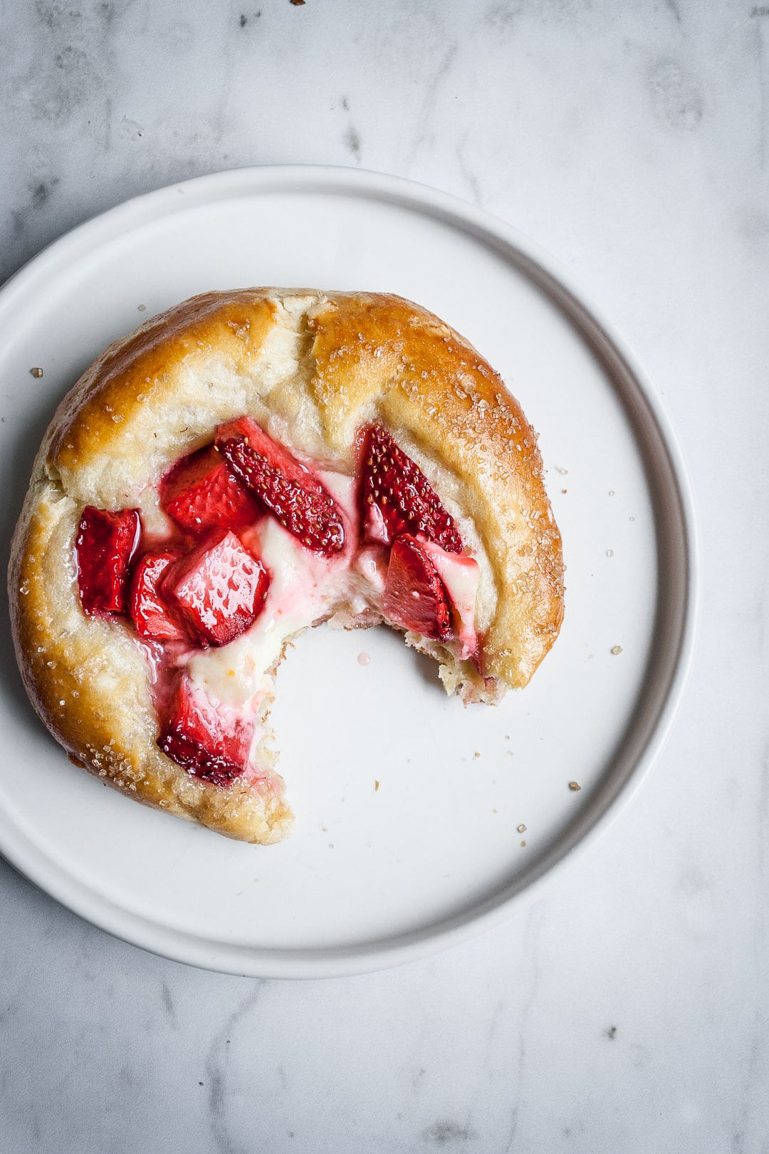 Close up of strawberry cream cheese brioche pastry on a white plate and marble background