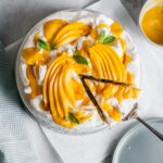 Meringue cake with mangoes on top with a slice being lifted out to put on a plate