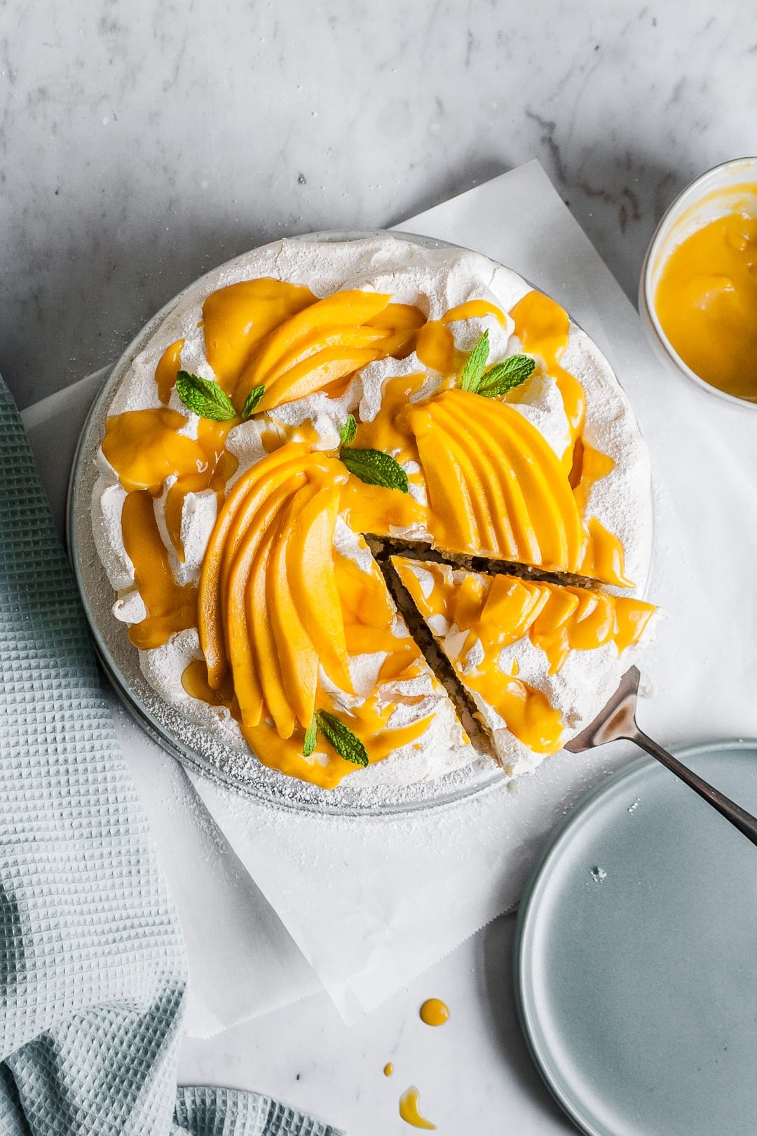 Meringue cake with mangoes on top with a slice being lifted out to put on a plate