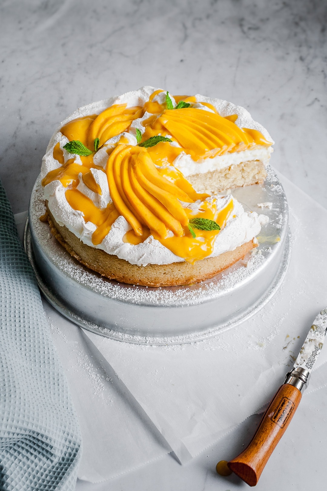 Angled view of coconut meringue cake with slices missing on a marble background