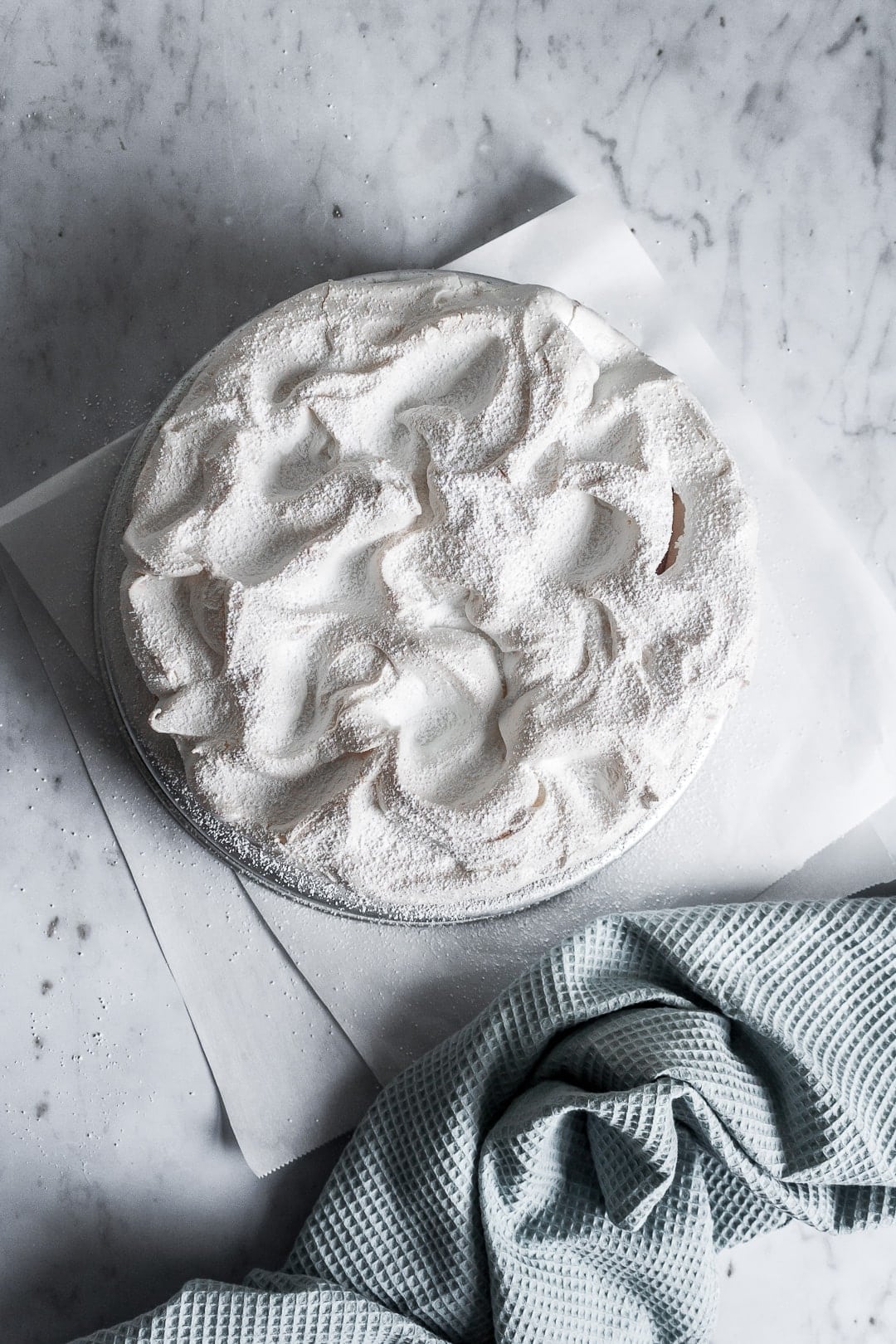 Top view of baked meringue covering a layer cake - on a marble background with parchment paper underneath