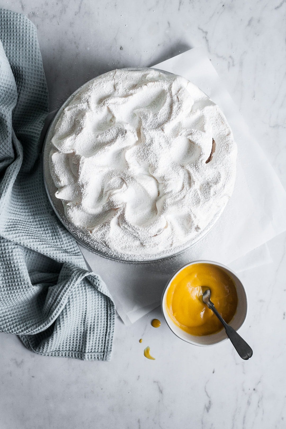 Top view of meringue layer of coconut meringue layer cake with bowl of mango sauce and blue towel nearby