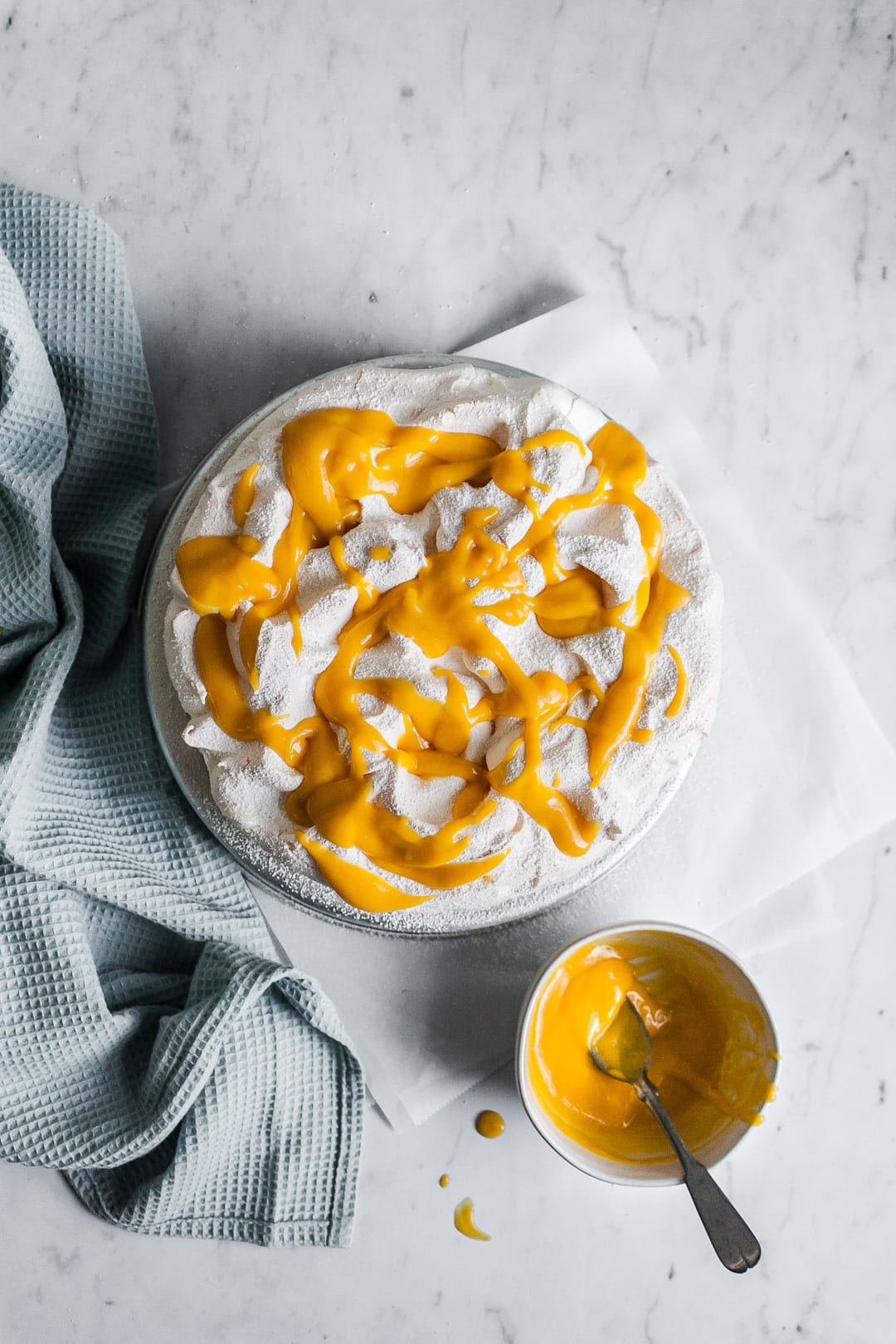 Meringue cake with mango sauce drizzled on top; small bowl of mango sauce next to cake