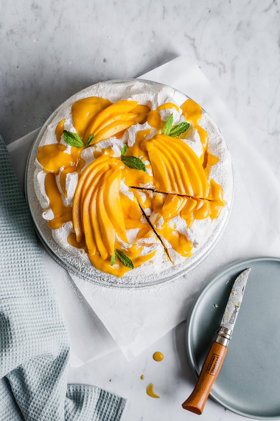 Meringue cake with mangoes on top with slice cut out of it and knife resting on plate nearby