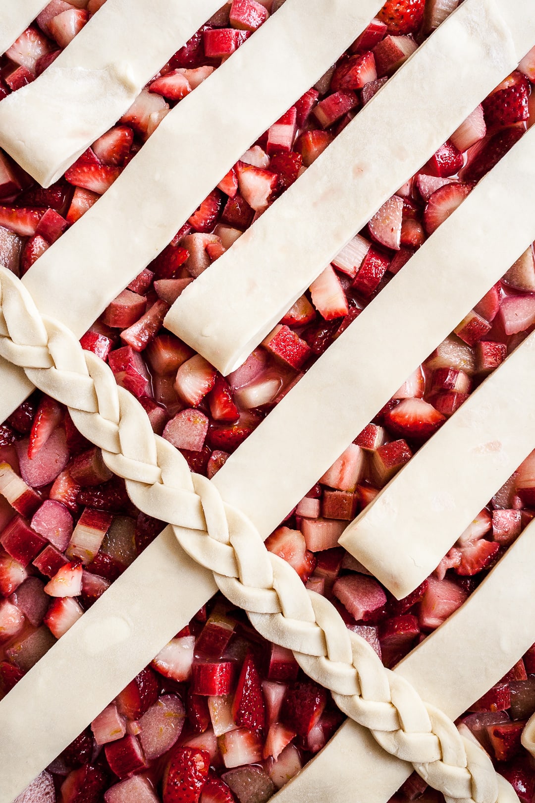 Close up of strawberry rhubarb pie filling with lattice dough strips and braid angled on top