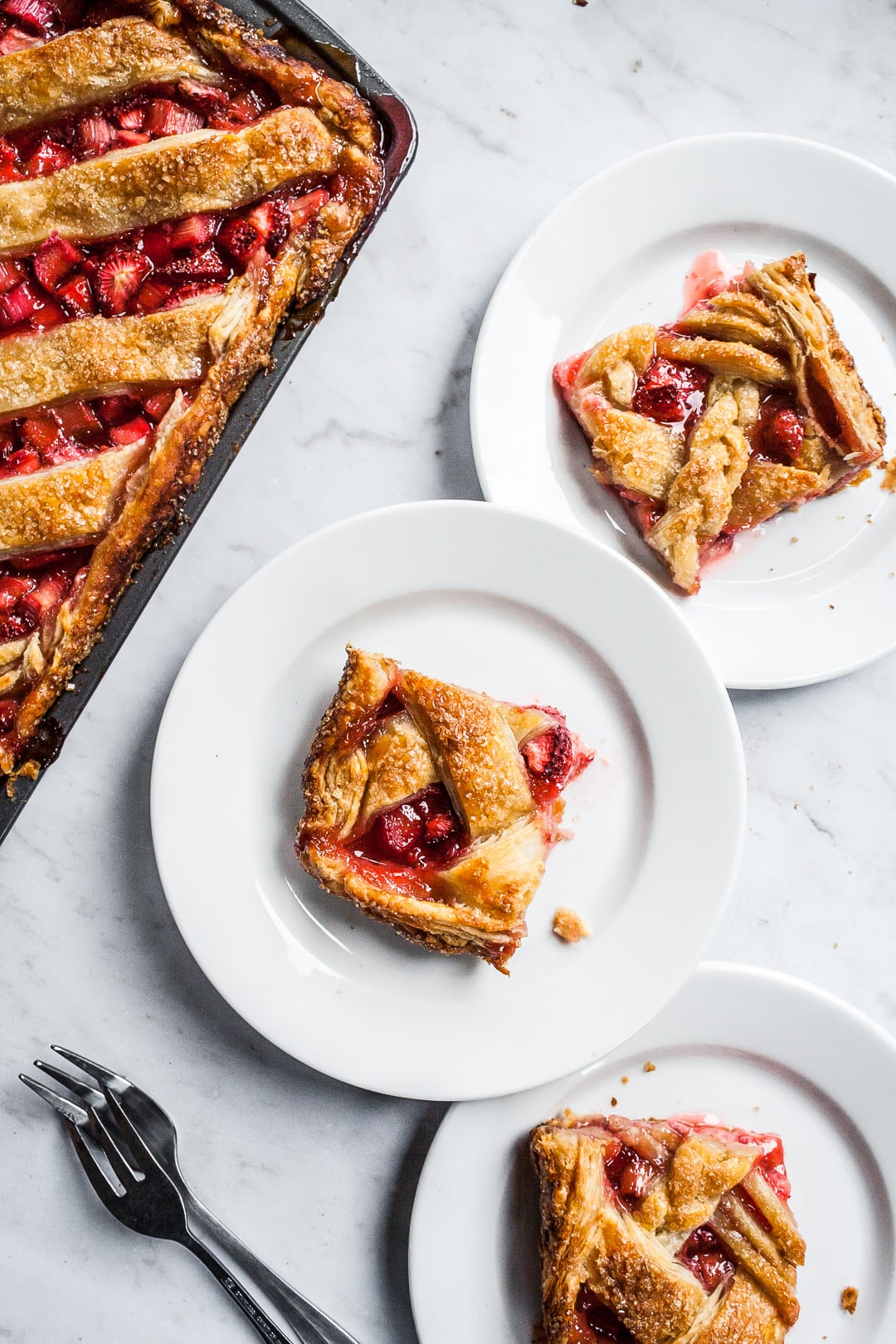 Slices of slab pie on white plates next to a sheet pan of slab pie