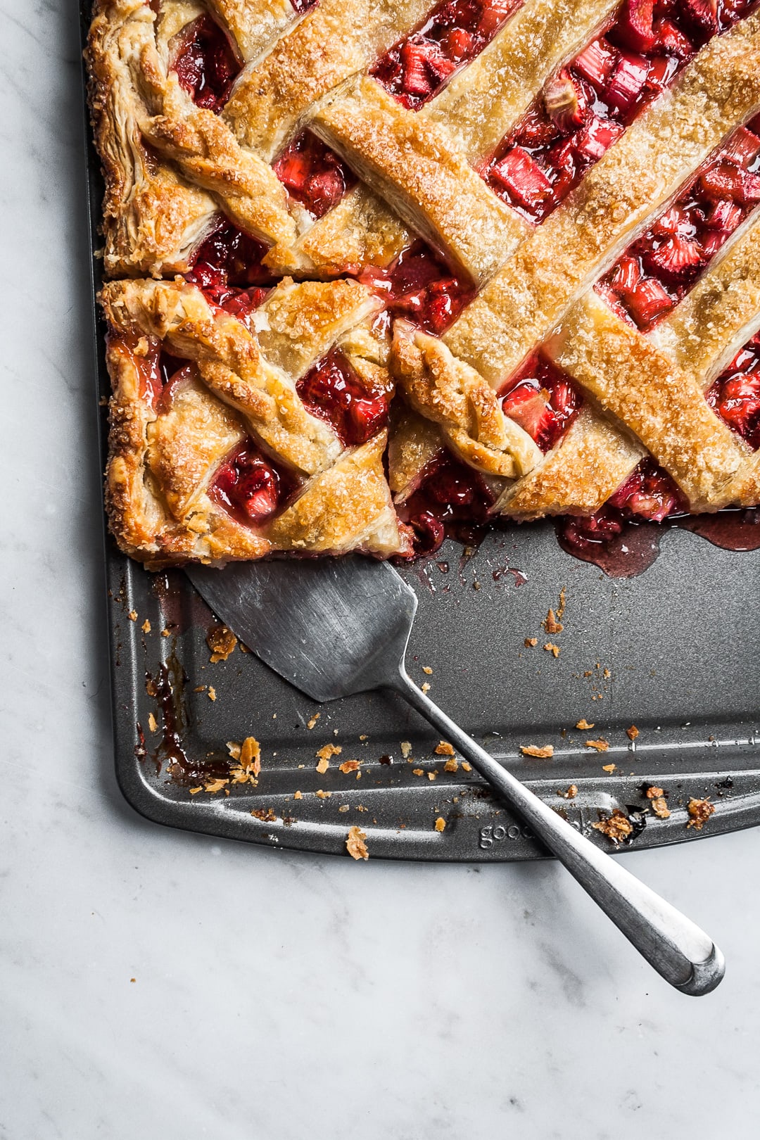 Baked strawberry rhubarb slab pie with a piece cut and being lifted by a serving utensil