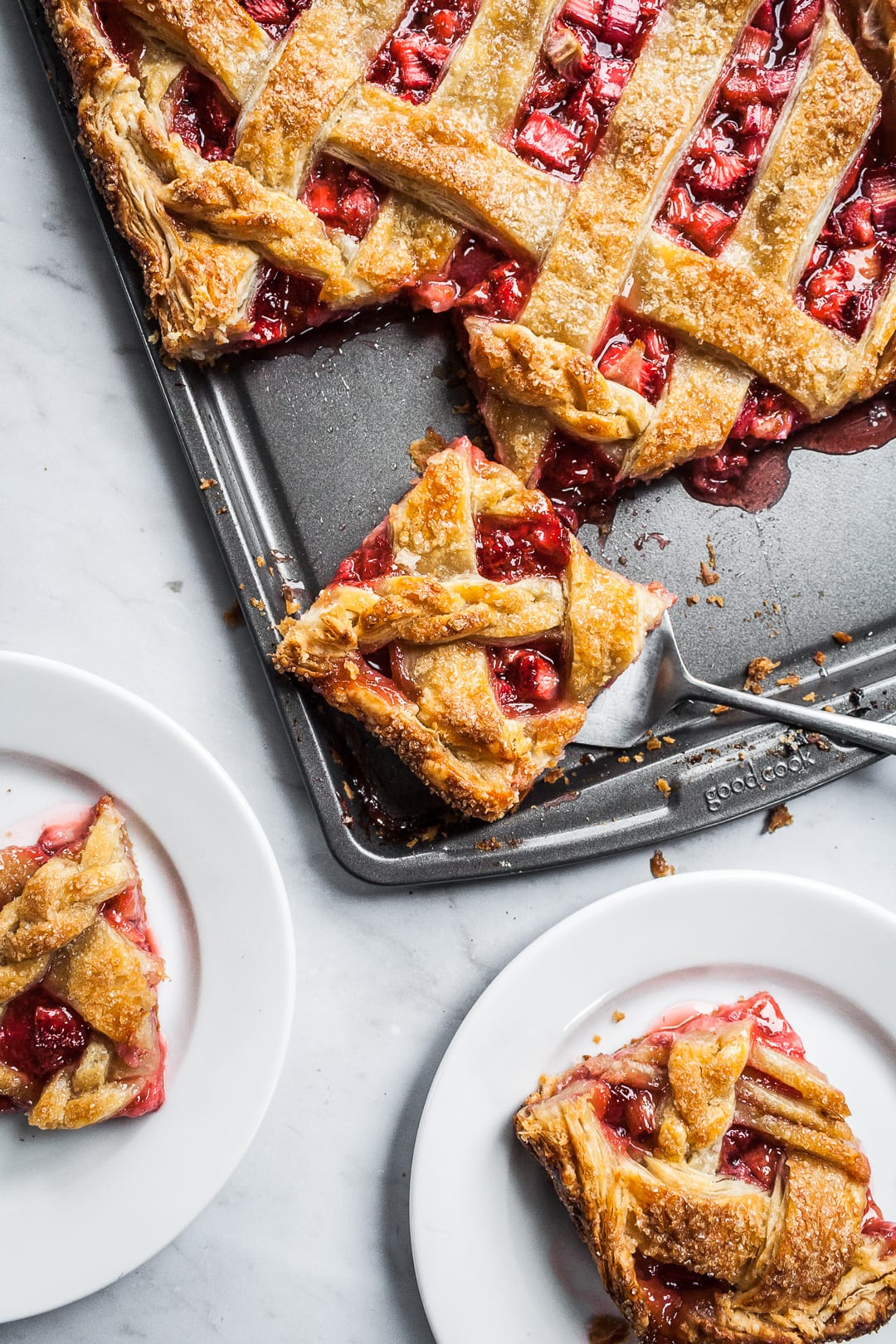 Baked strawberry rhubarb slab pie with pieces being served onto white plates