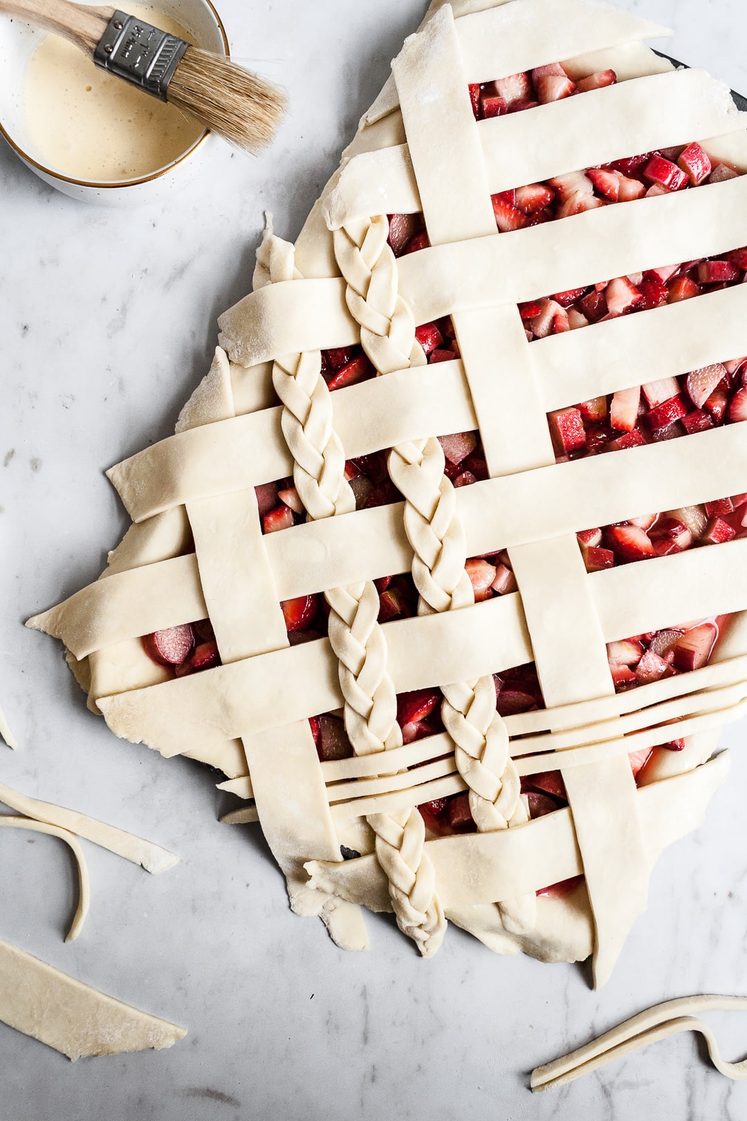 Top view of unbaked strawberry rhubarb slab pie with angled woven lattice crust with braids on a white background