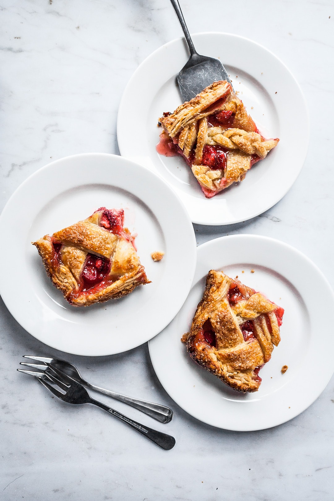 Three square slices of slab pie on white plates and a marble background with forks and serving utensil nearby