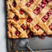 A slice of strawberry rhubarb slab pie being cut out on a baking sheet.