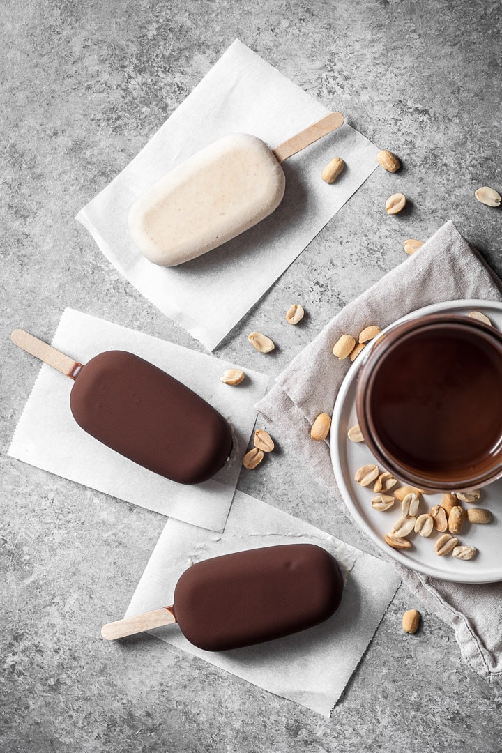 Chocolate dipped peanut butter ice cream bars on parchment paper squares on a grey background