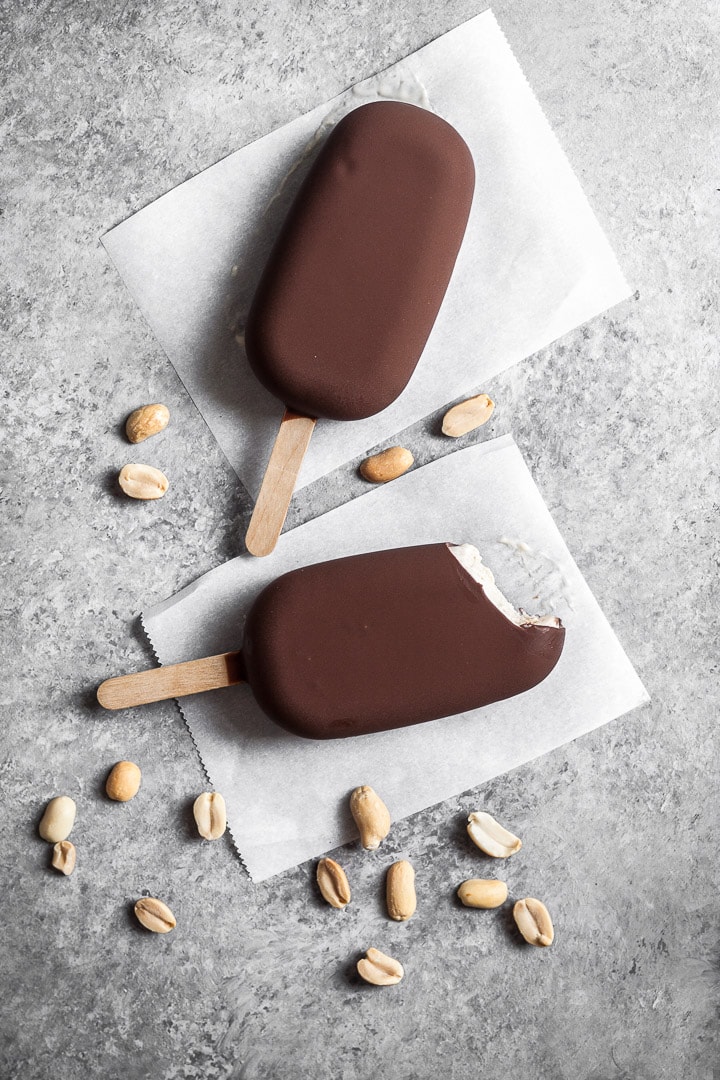 Chocolate dipped peanut butter ice cream bars on a grey background with peanuts sprinkled nearby
