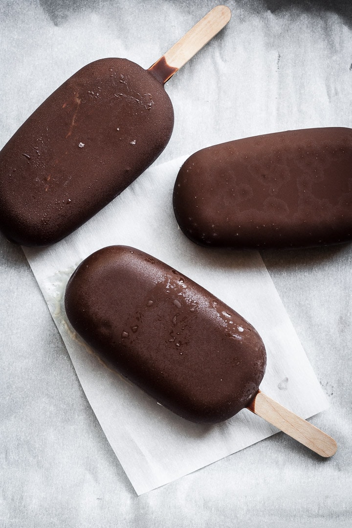 Three chocolate dipped ice cream bars on parchment paper