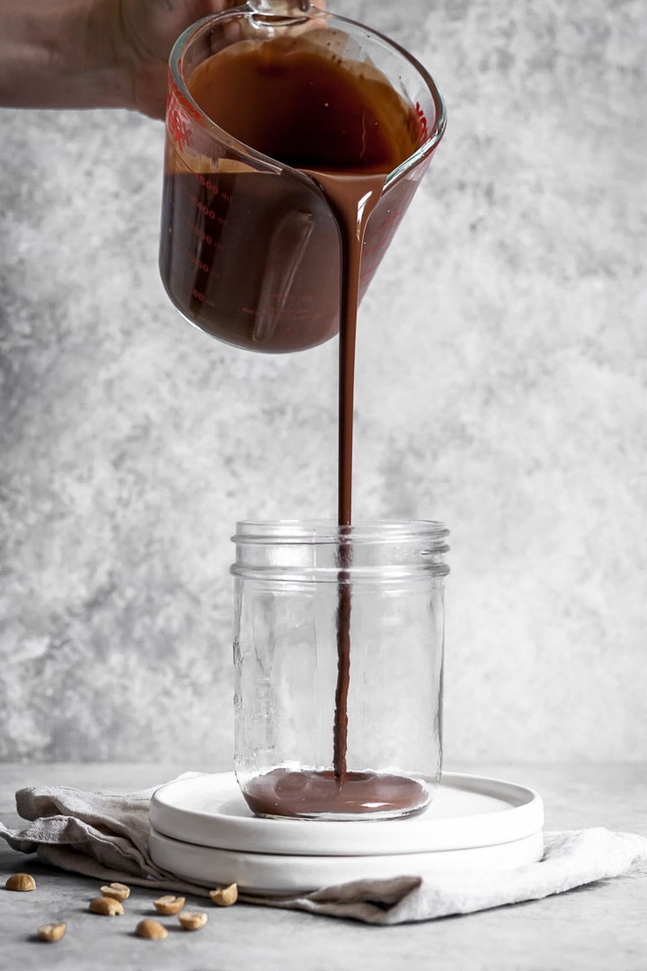 Melted chocolate being poured into a jar with a grey background behind