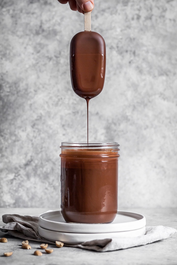 Hand dipping peanut butter ice cream bar into chocolate