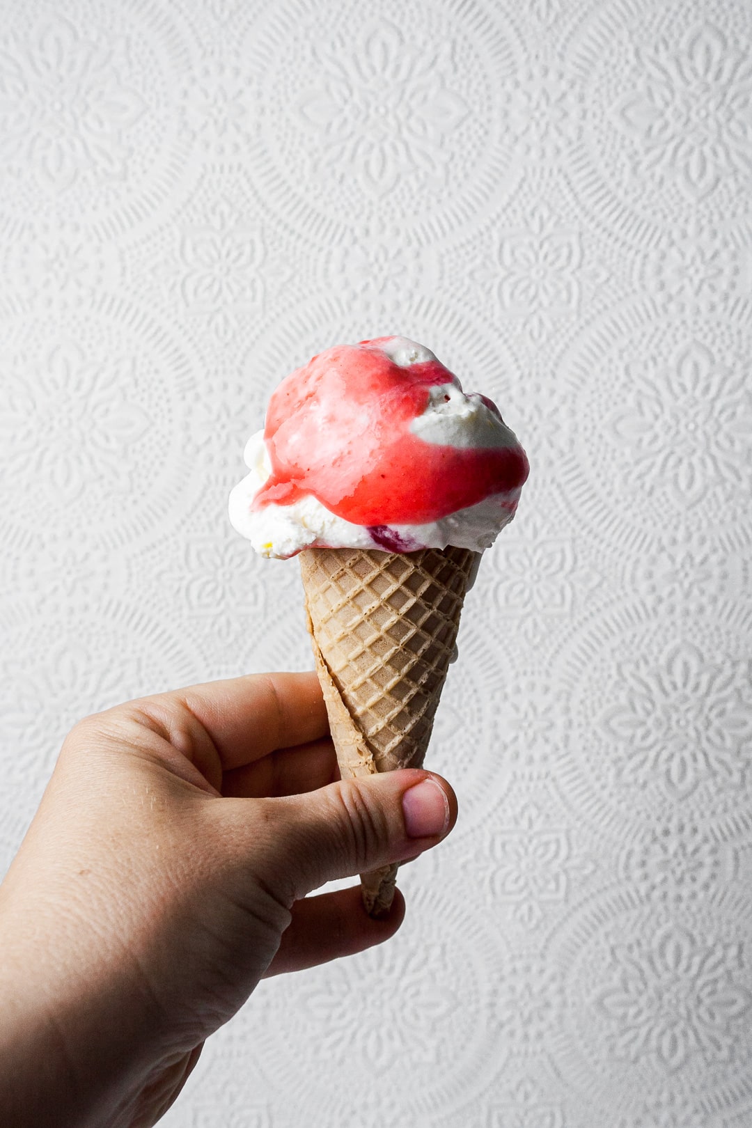 Hand holding lemon mascarpone ice cream with currant sauce on top