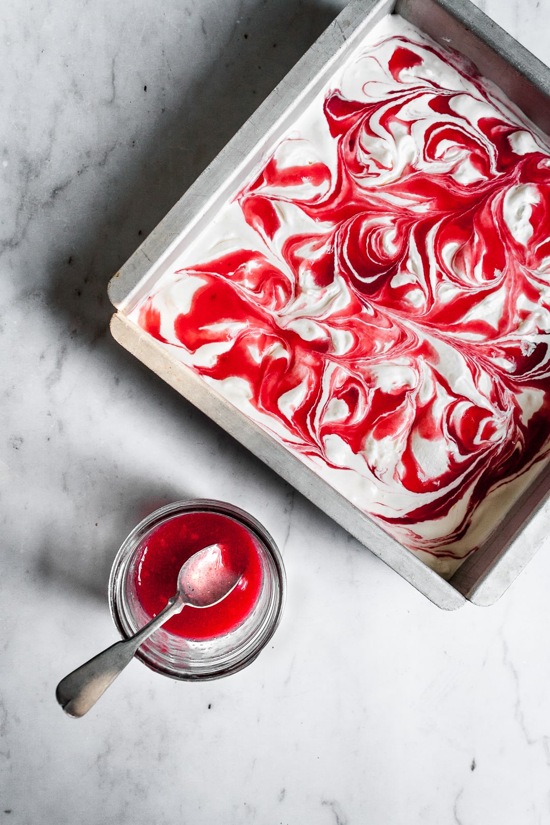 Lemon Mascarpone Ice Cream with Currant Swirl in a square metal pan with a jar of currant sauce and spoon nearby