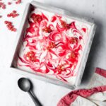 Lemon Mascarpone Ice Cream with Currant Swirl in a square metal pan with loose bunches of currants strewn over the top and nearby