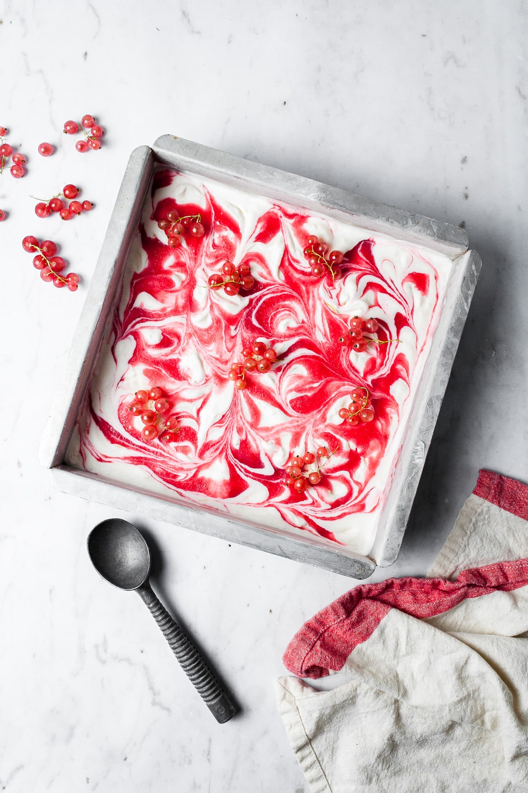 Lemon Mascarpone Ice Cream with Currant Swirl in a square metal pan with loose bunches of currants strewn over the top and nearby