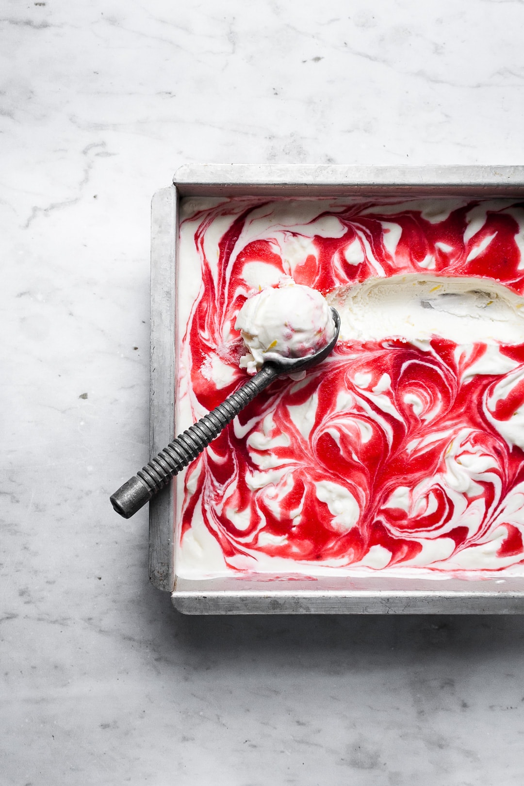 Square metal pan with red and white swirled ice cream and the marks of a scoop being removed with a vintage ice cream scoop