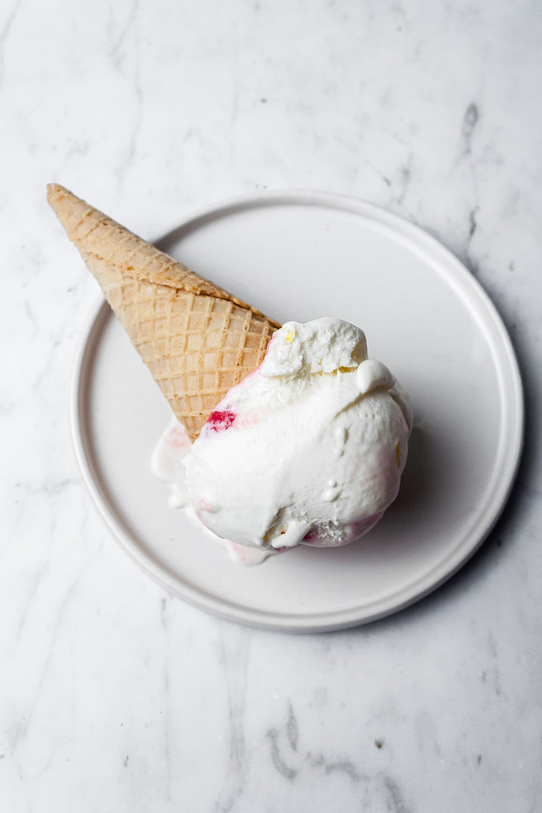 Sugar cone with scoop of ice cream on a white plate and marble background