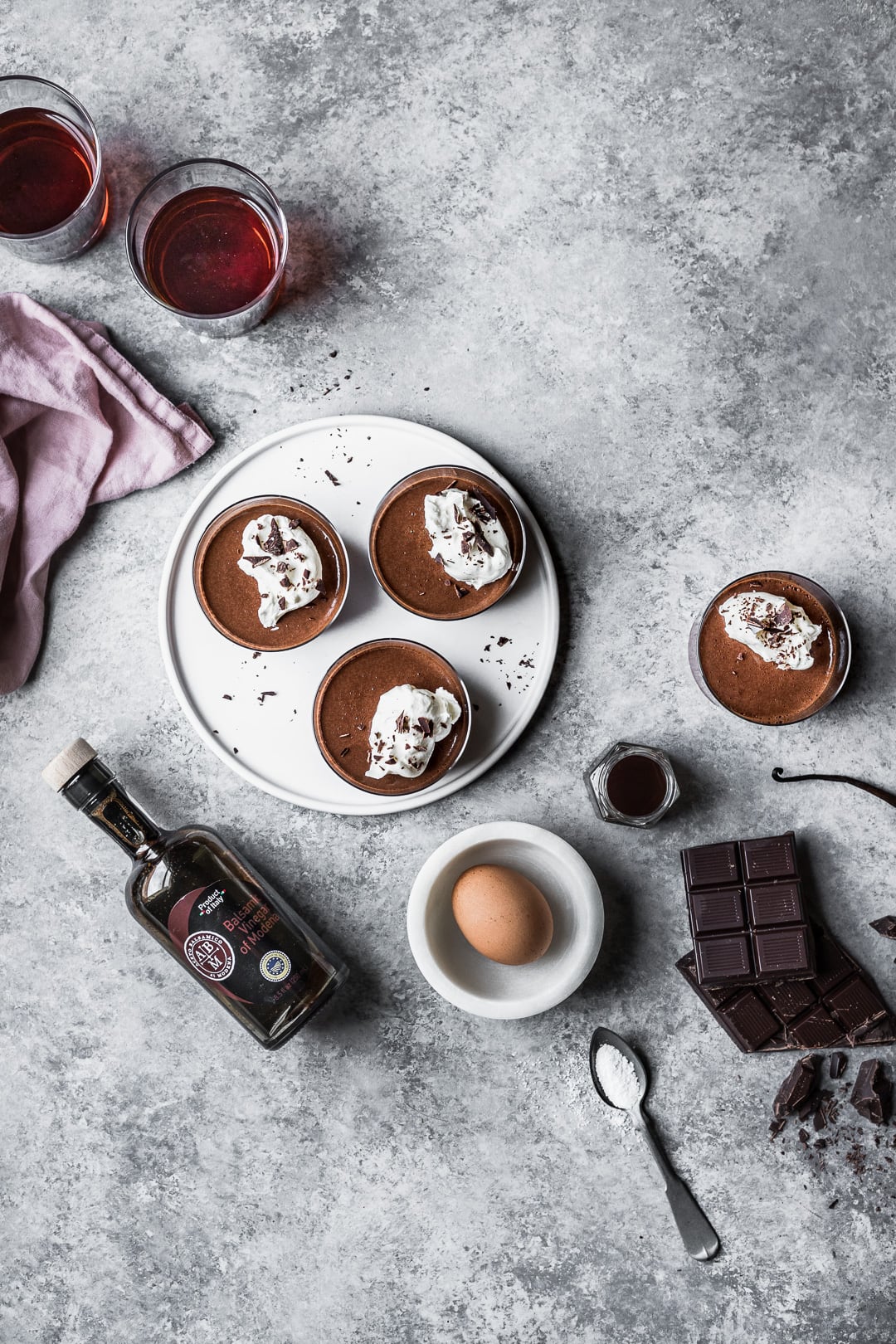 Chocolate pots de creme on a grey background surrounded by the recipe ingredients