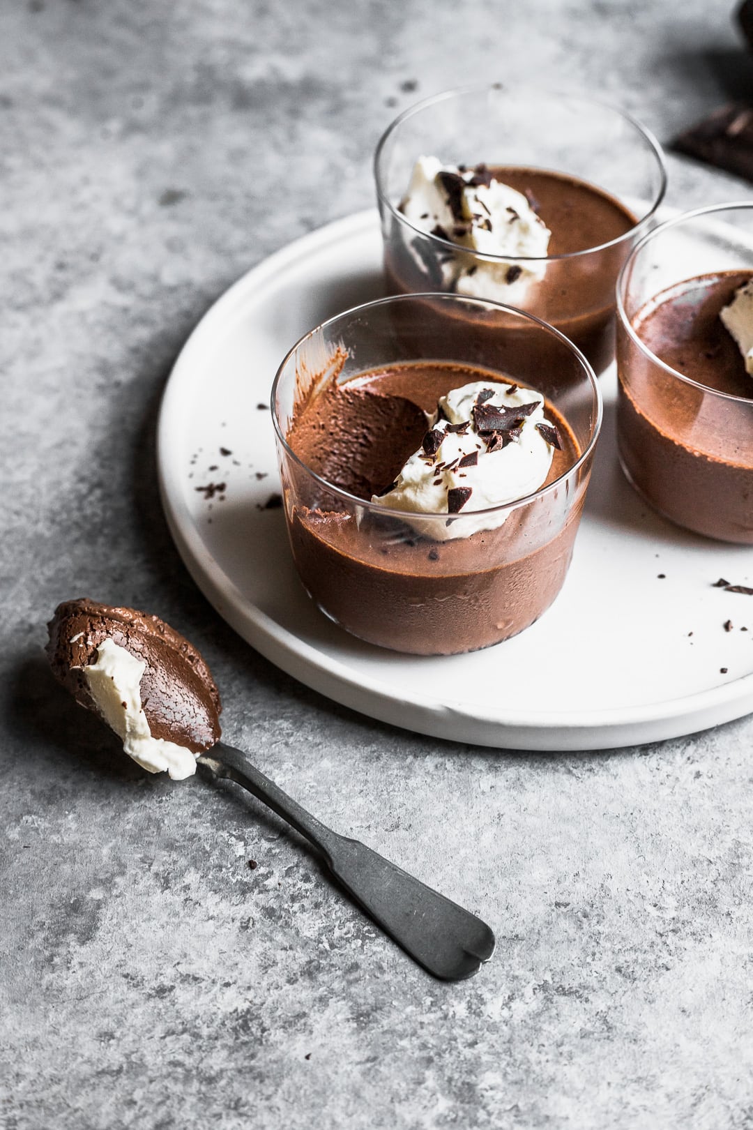 Chocolate dessert in glasses on a white plate and grey background with a spoon resting nearby