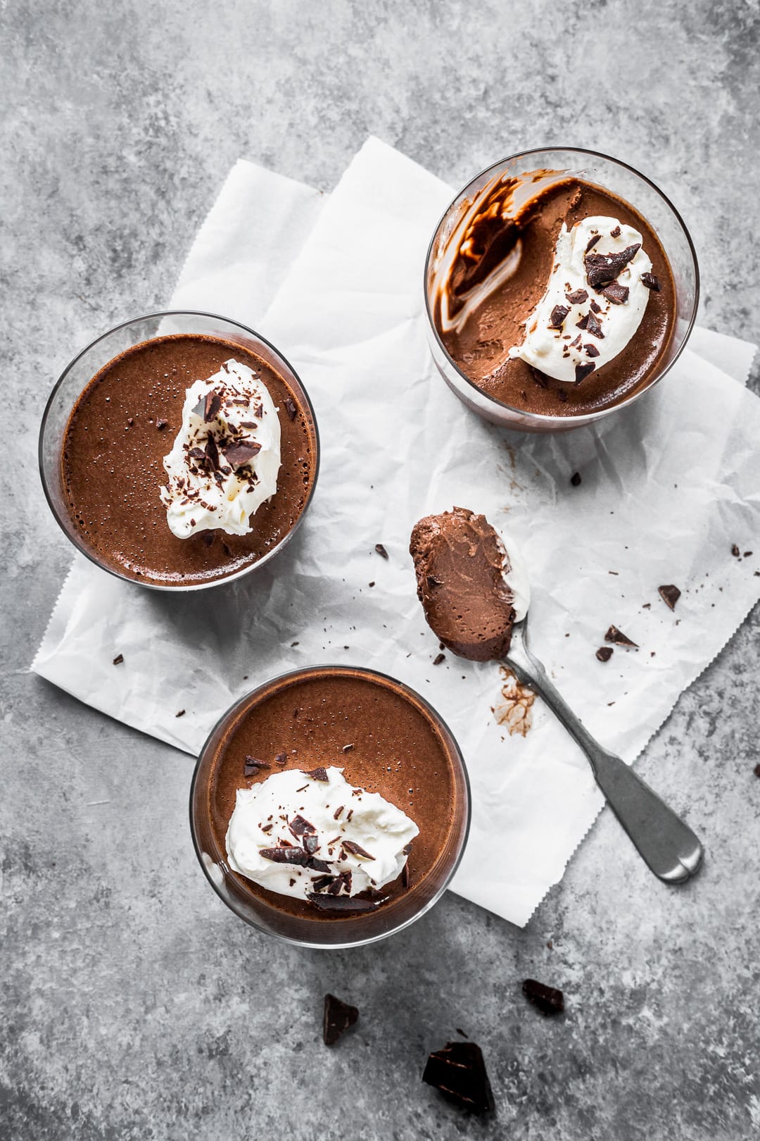 Three chocolate pots de creme on white parchment paper and a grey background