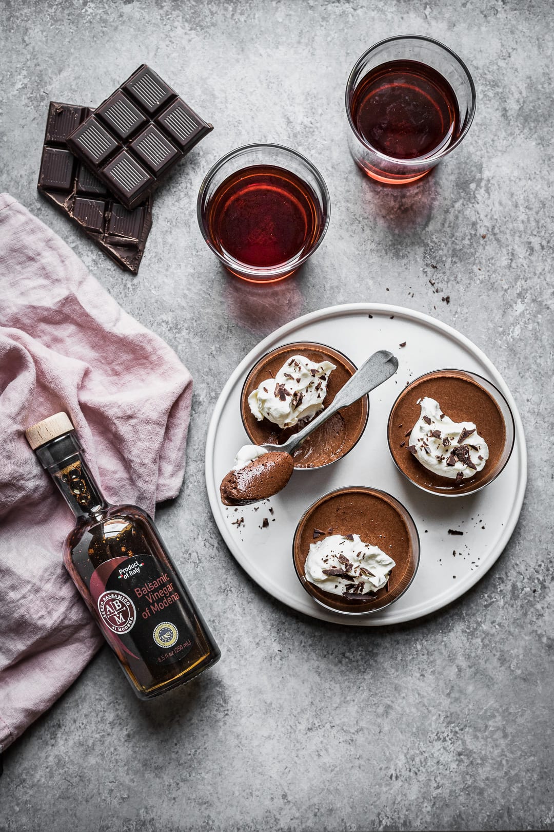 Chocolate pots de creme on a grey background with bottle of balsamic vinegar resting nearby on a pink linen napkin