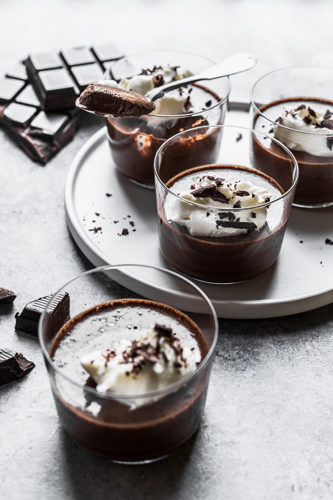 Angled backlit view of chocolate pots de creme on a white plate and grey background