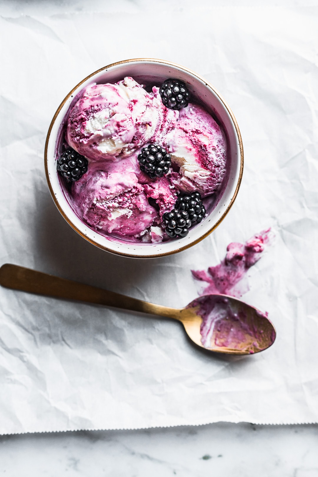 Bowl of honey blackberry mascarpone ice cream scoops with blackberries on top and gold spoon nearby