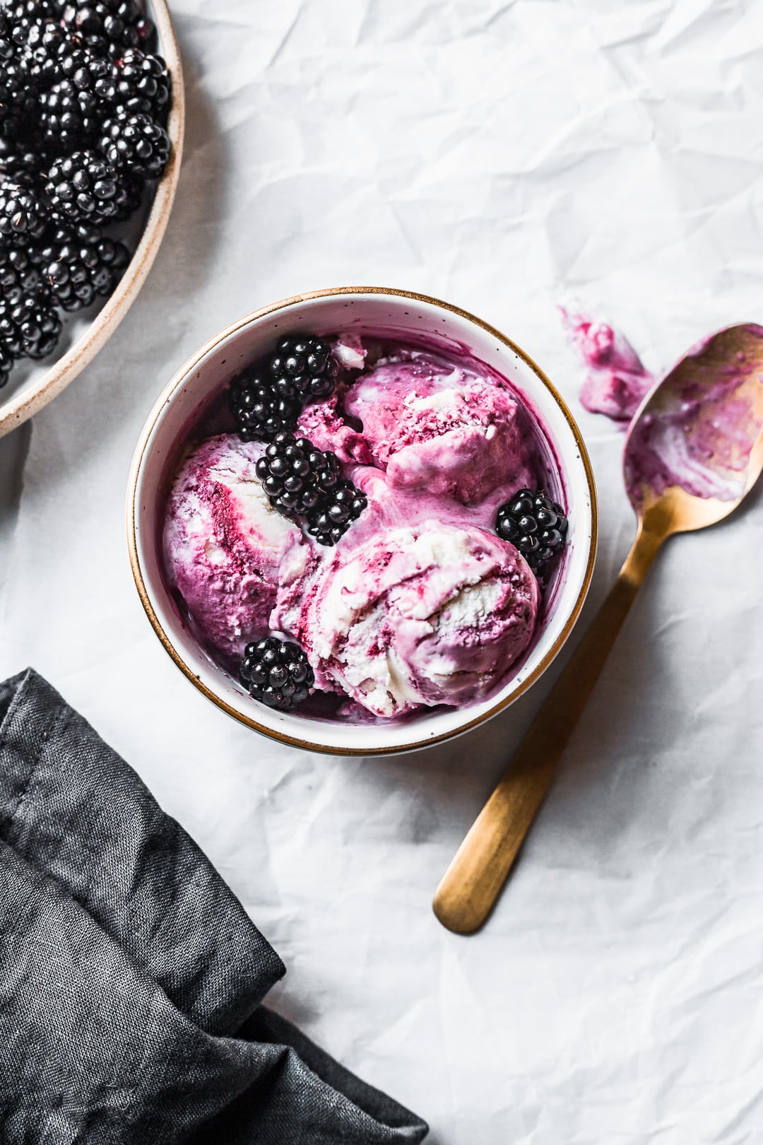 Bowl of purple and white ice cream scoops topped with blackberries and gold spoon nearby