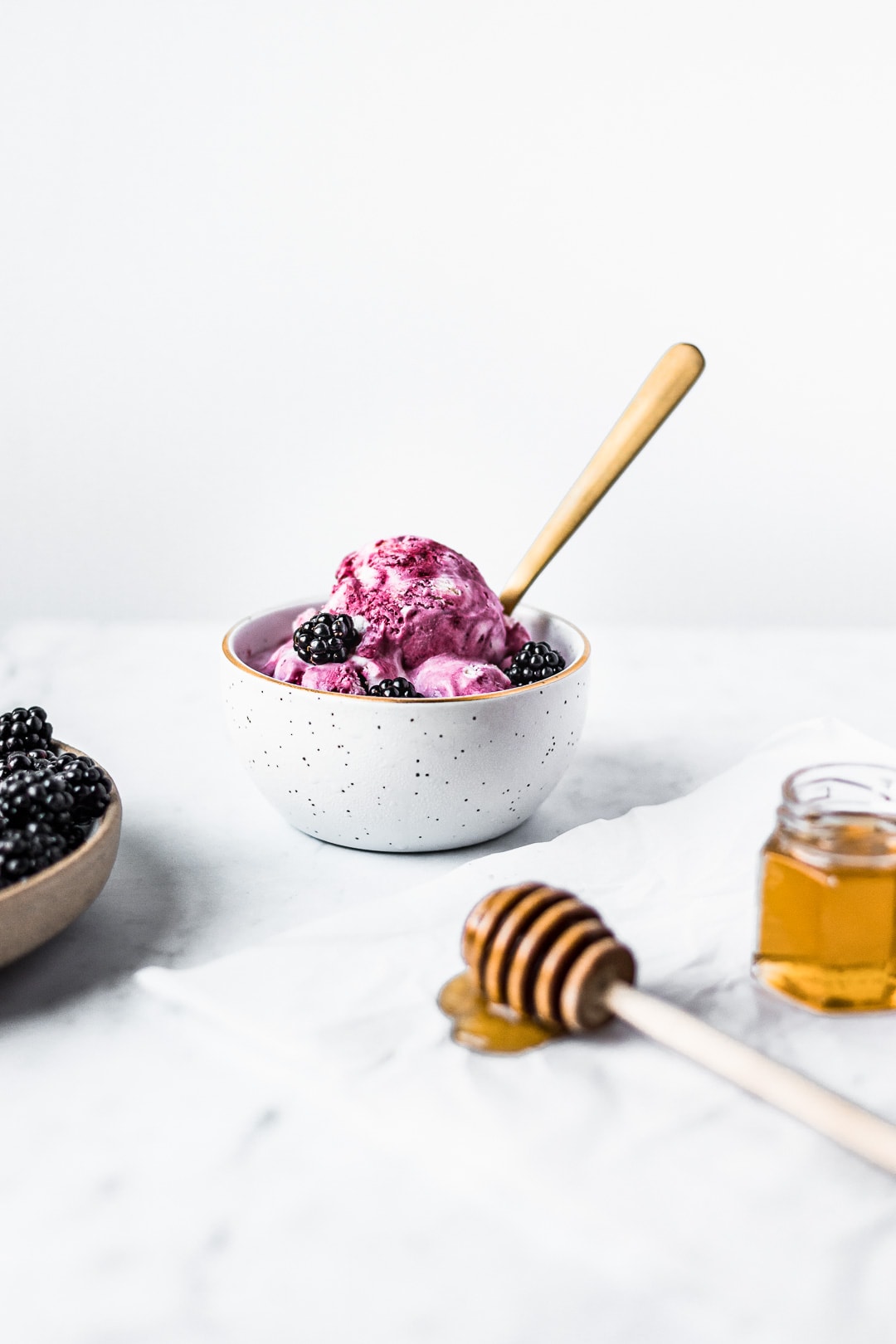 Front view of honey blackberry mascarpone ice cream scoops in a bowl with blackberries and honey in foreground