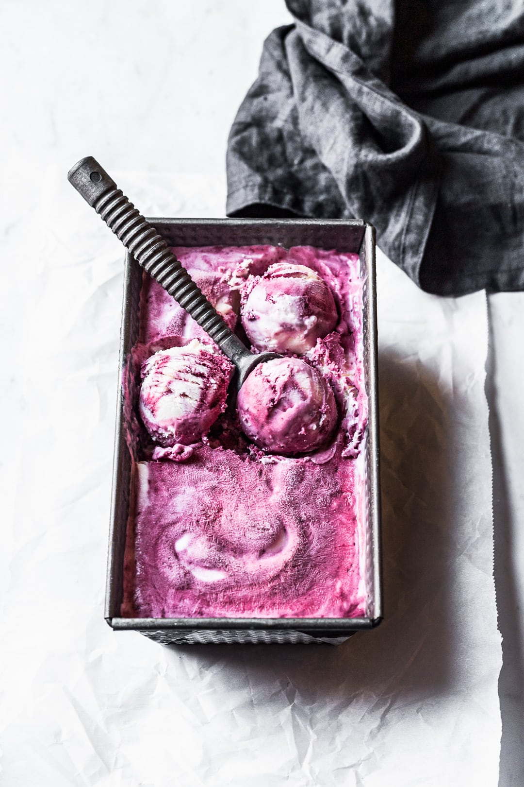 Angled view of purple and white swirled ice cream with three scoops shaped and ice cream scoop resting on container