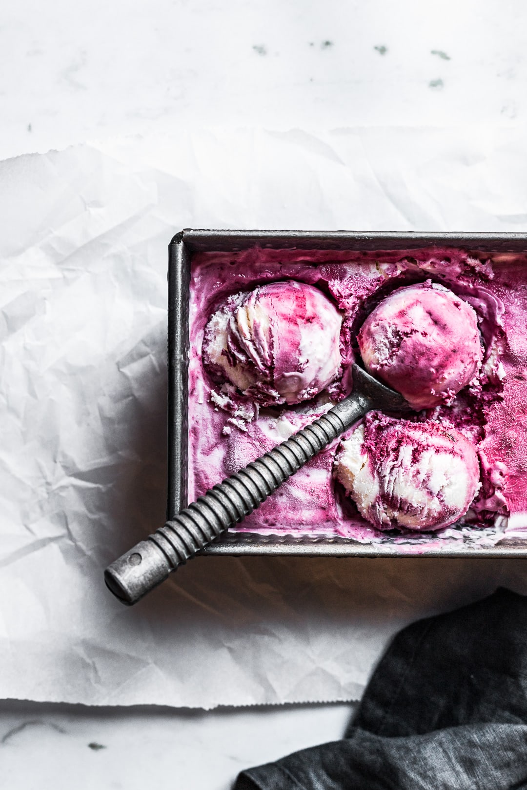 Closeup of three scoops of purple and white blackberry mascarpone ice cream in a container with the scoop resting on top